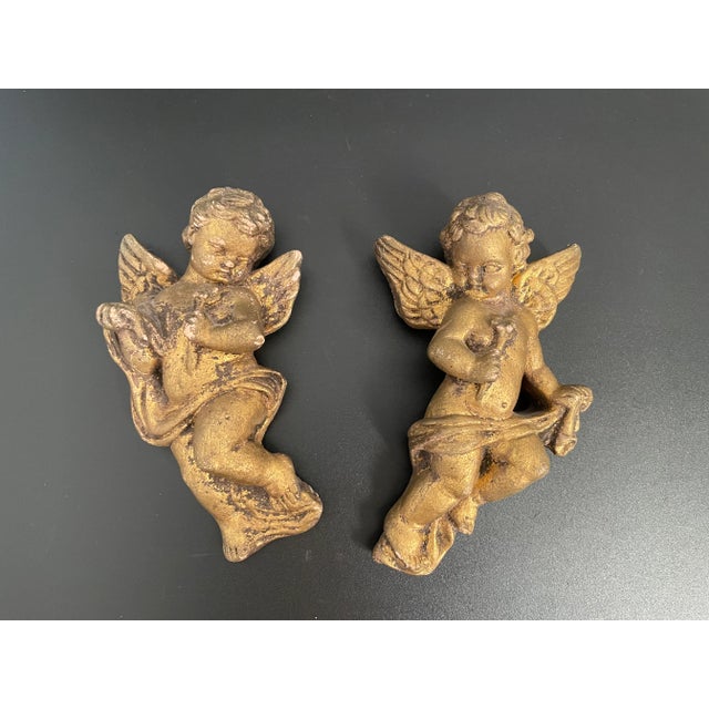 Presenting a pair of gilt gesso cherub wall hangings, each cherub holding a floral spray in hand. Dating back to the early...
