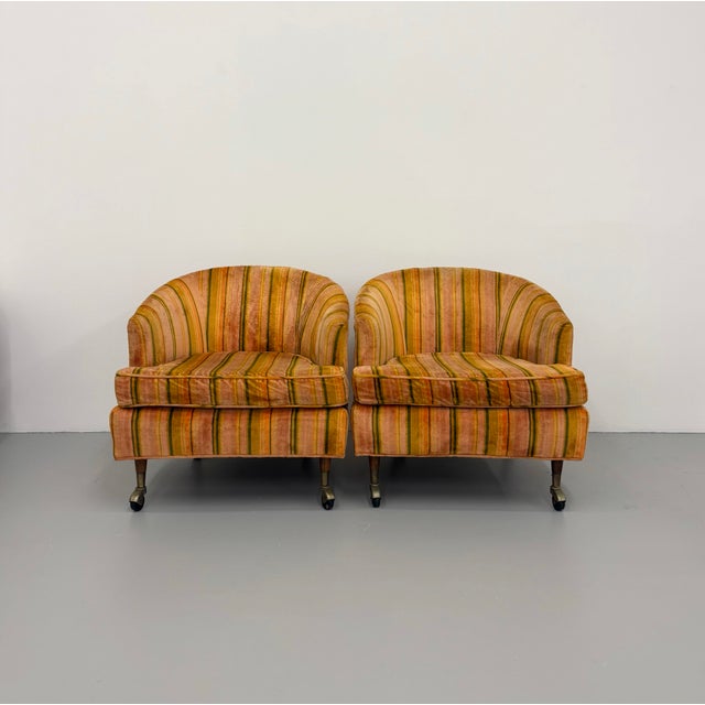 A charming pair of vintage barrel back lounge chairs featuring softly curved silhouettes upholstered in warm earth-toned...