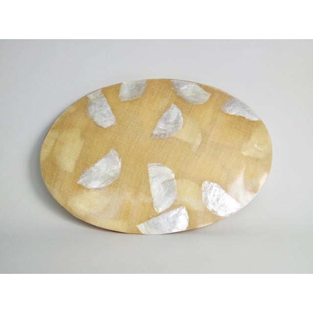 A set of six oval resin, capiz shell and burlap placemats. Handmade in the 1970s, each placemat was crafted with capiz...