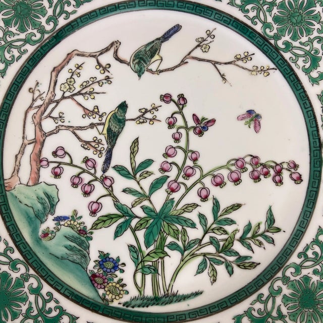 A beautifully painted porcelain plate featuring a central scene of birds perched among flowering branches, with...