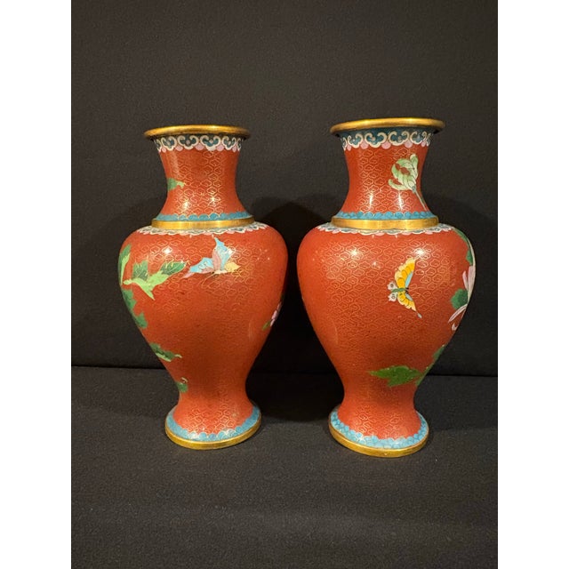 This hand made pair of Cloisonné vases feature richly detailed pink and blue flowers on a crimson background. A lone...
