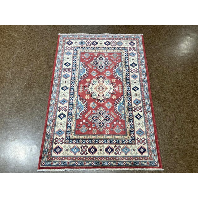 Hand-knotted Pakistani Kazak wool rug featuring a red field with bold central geometric medallions and stylized tribal...