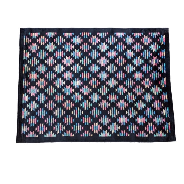 Black silk rug with geometric designs in light pink, yellow, blue, and green, creating diamond-shaped patterns with an...