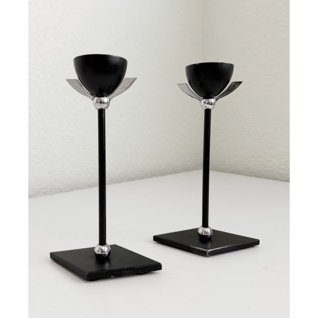 A pair of 1980s postmodern Memphis style candle holders. Featuring black metal, diamond-shaped base, and winged chrome...