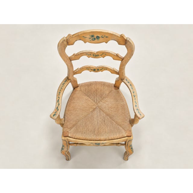 This set of two vintage ladderback armchairs features softly curved silhouettes, hand-painted floral detailing, and woven...