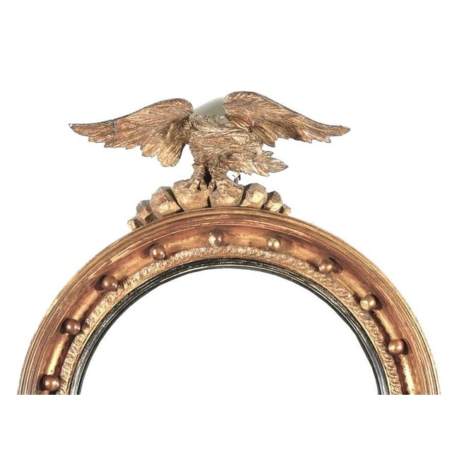 19th Century Regency or Federal Carved Giltwood Convex Bullseye Mirror with Eagle Pediment. Mirror is carved in giltwood...