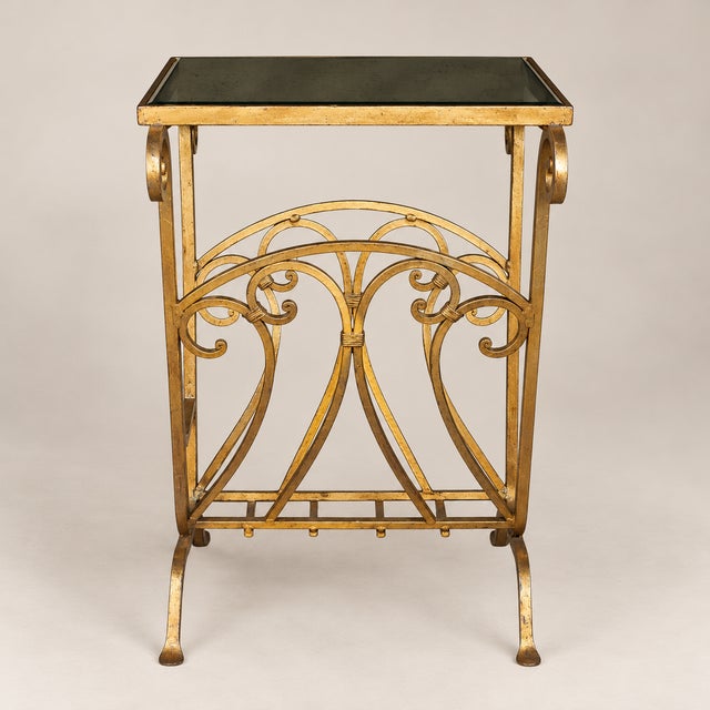 An elegant Hollywood Regency gilt metal side table with beveled mirrored glass top and an integrated magazine rack....