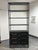 Design Plus Gallery presents a Honshu Rack by HD Buttercup. This tall etagere has a black metal frame, open shelving, and...
