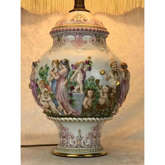 A richly detailed Italian Capodimonte porcelain lamp, adorned with sculpted mythological figures, cherubs, and classical...