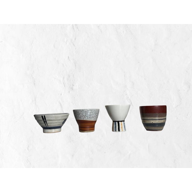 A thoughtfully curated collection of four Japanese studio pottery vessels including sake cups and a petite pour form, each...