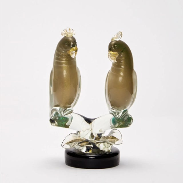 The hand blown Sculpture depicts a pair of parrots poised upon twisted branches. The artist has represented the birds in...
