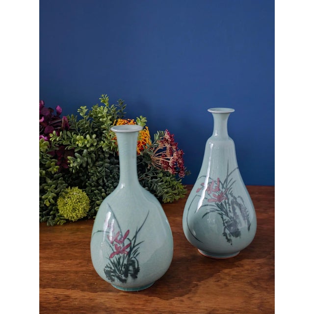 Beautiful pair of vintage Korean celadon vases, each showcasing a graceful hand-painted red orchid and black foliage motif...