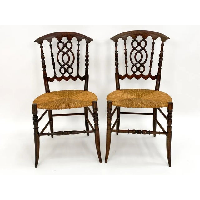 A pair of delicate saber leg side chairs with rush seats, nicely carved and interlaced back splats and turned legs and...