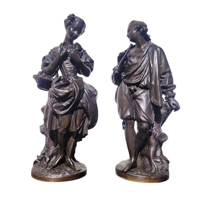 Bronze figures with a brown patina depicting a couple dressed in 18th-century fashion: the young man, leaning against a...