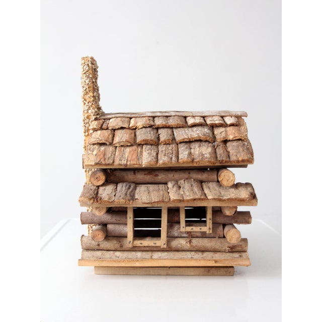 A charming vintage folk art sculpture depicting a rustic woodland log cabin, meticulously handcrafted from natural...