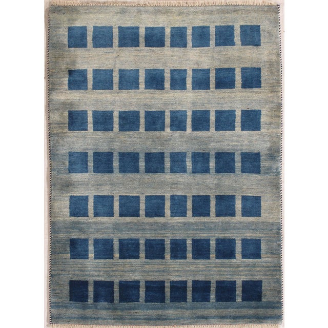 Hand-knotted Persian Gabbeh wool rug featuring rows of deep blue square motifs arranged across a softly striated gray-blue...