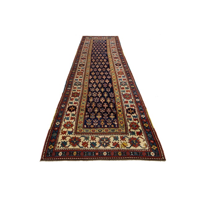 This handcrafted Kazak wool rug showcases a vibrant blue palette with delicate red, yellow, and beige accents. It is...