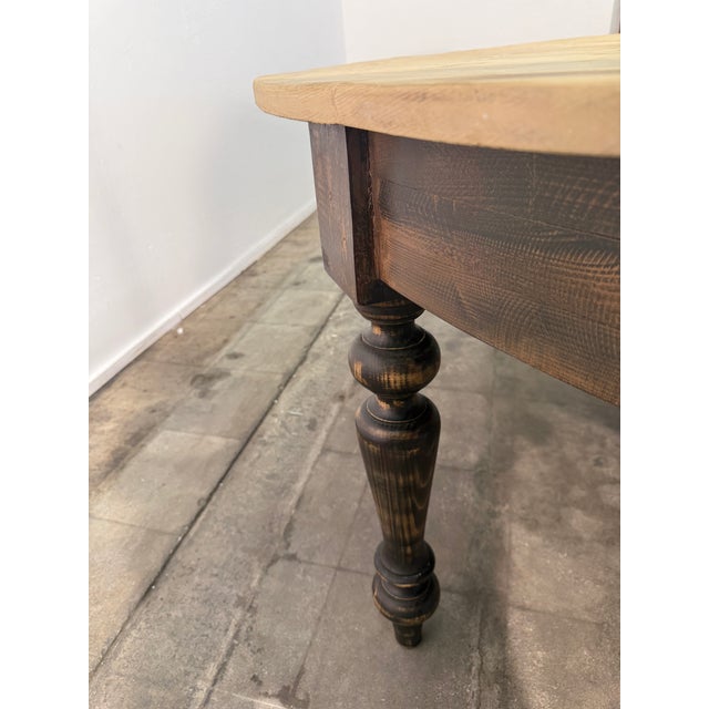 Large round dining table featuring a natural pine plank top with visible grain, knots, and a beautifully aged finish. The...