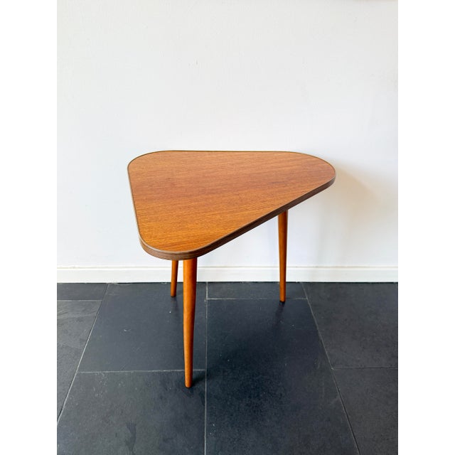 This asymmetrical wooden side table is designed in a mid-century modern style, with a three-sided top, softly rounded...