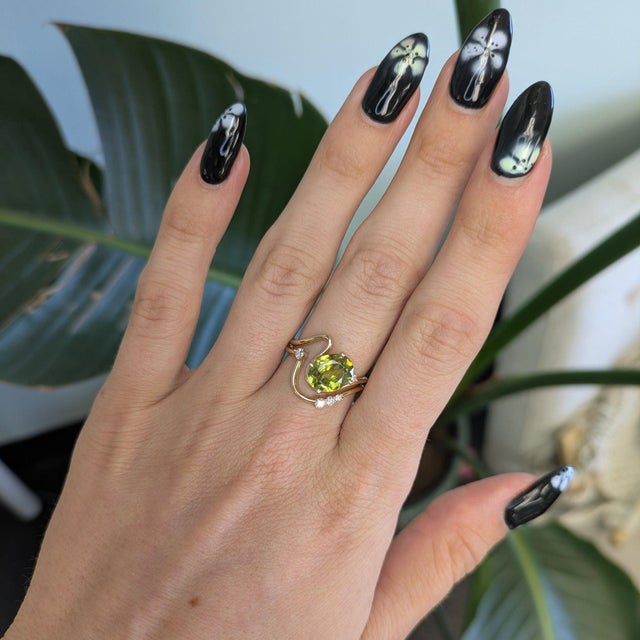 A natural sphene blazes with green-gold fire that surpasses a diamond's at the heart of this ring, framed by earth-mined...