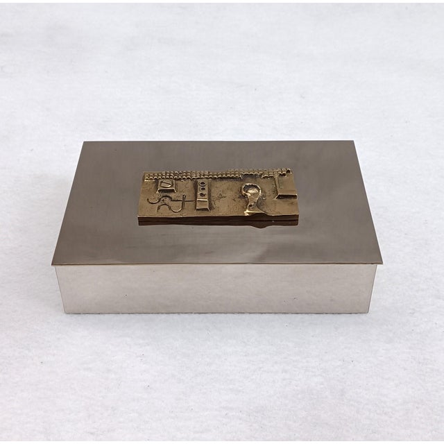 Elegant chromed metal box with a lid decorated with a carved gilt bronze plaque. Made in Italy in the 1970s/1980s. A...