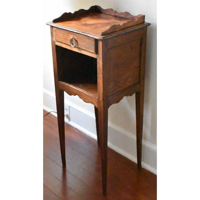 French Fruitwood nightstand, early 1800s. A unique scalloped, molded edge top rests on a central drawer with a brass ring...