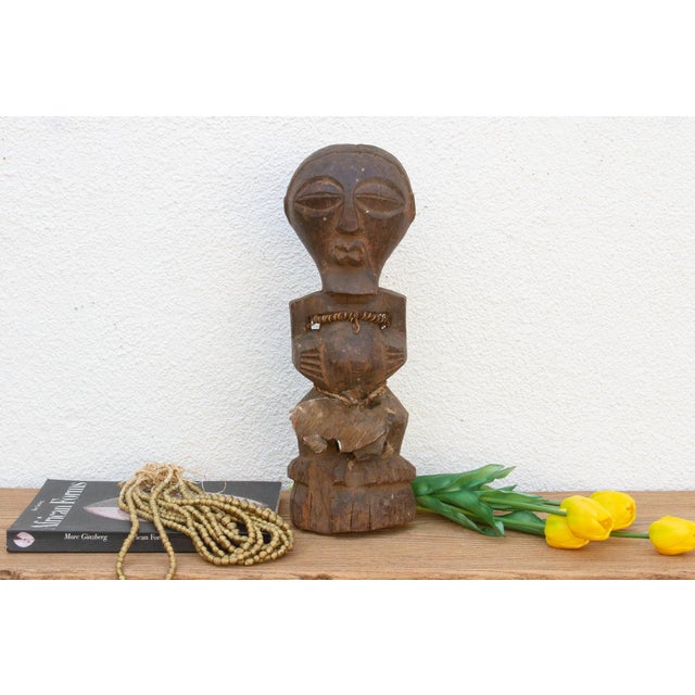 This compelling African power figure, carved from wood and adorned with metal embellishments, exudes an aura of strength...