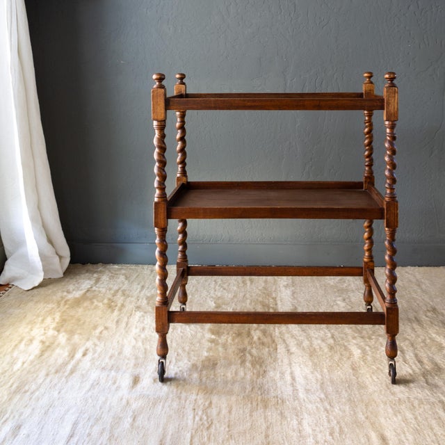 An antique English Edwardian tea cart or bar cart features a slender frame with graceful, barley twist legs topped with...