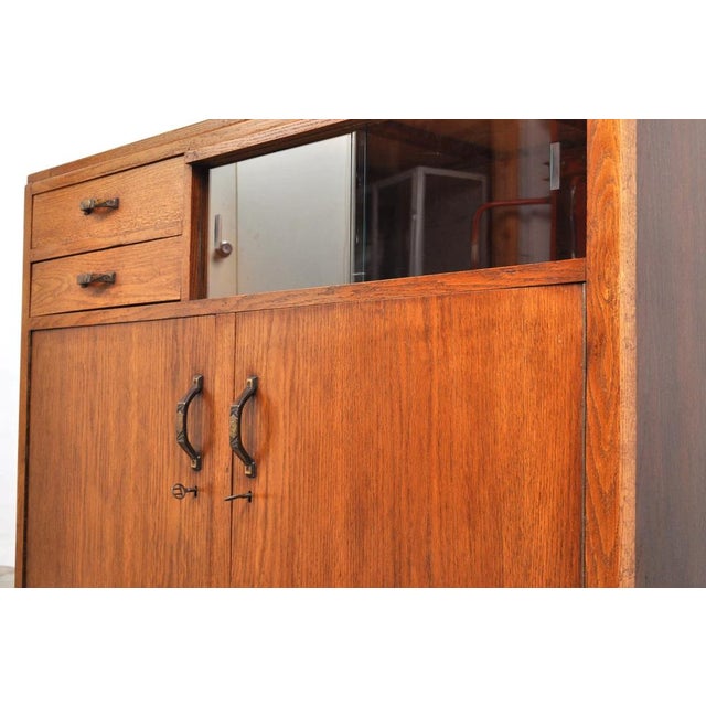 Sleek Art Deco cabinet. The oak cabinet, from the 1920s, features two doors with working locks, two drawers, and a display...