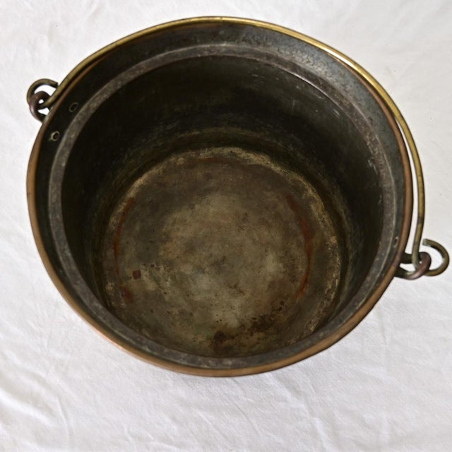 An antique French copper cooking pot with a forged iron carrying handle for suspending over the fire, dating to the second...