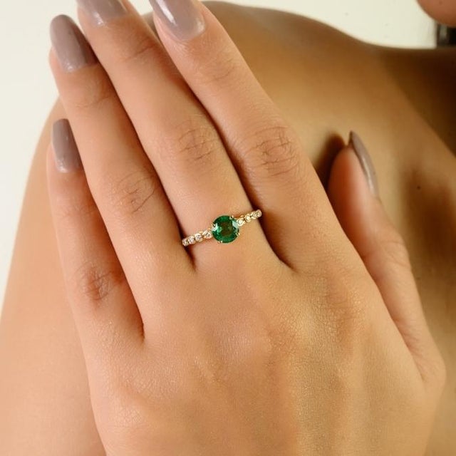 This certified 14K yellow gold ring featuring a vivid round-cut natural Zambian emerald weighing approximately 0.57...