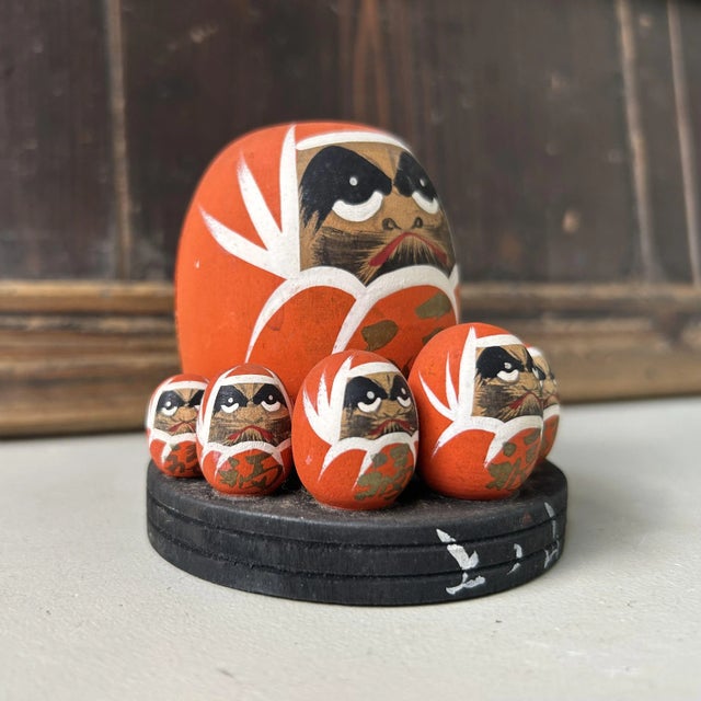 Charming wooden Daruma set featuring one large and eight small hand-painted Daruma figures arranged on a black wooden...