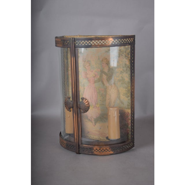 Brass vitrine wall lamp with curved glass, pierced fretwork and a fabric garden-scene panel depicting a lady in pink. Two...