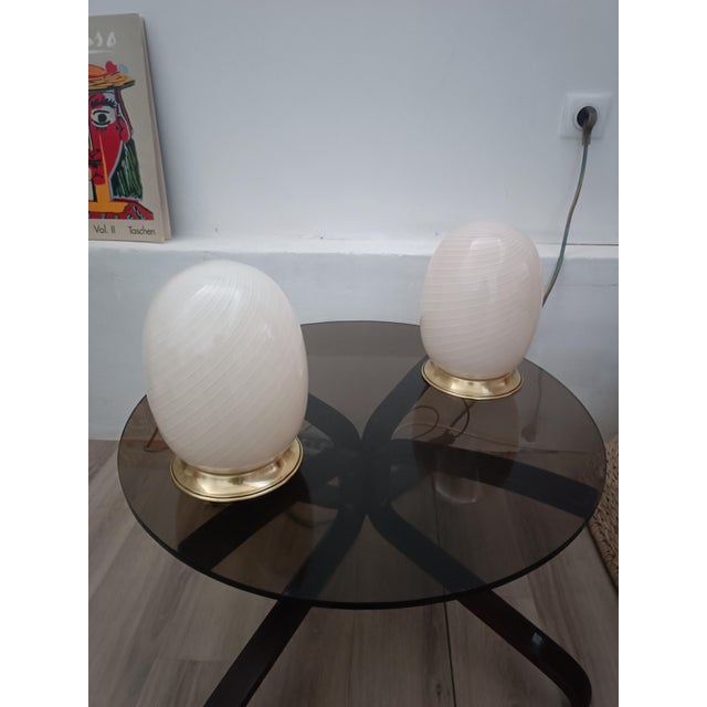 Beautiful pair of table lamps. Italy, 1970s. Brass base. Each lamp features a stunning egg-shaped tulip shade. Murano...