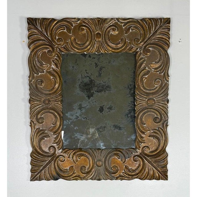 An Italian Baroque mirror dating to the early 19th century, featuring a richly carved wooden frame with deep scrolling...