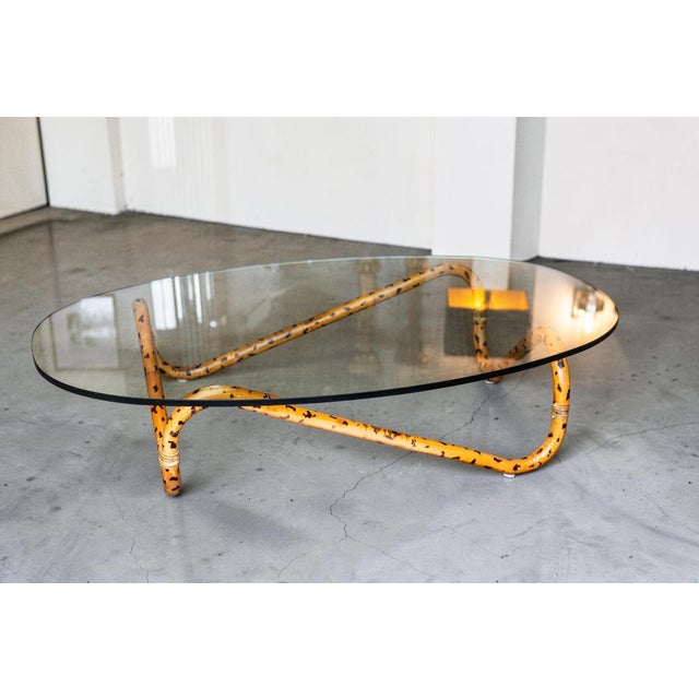 Distinctive tortoiseshell faux bamboo coffee table featuring a sculptural bent frame and oval glass top. Finished in a...