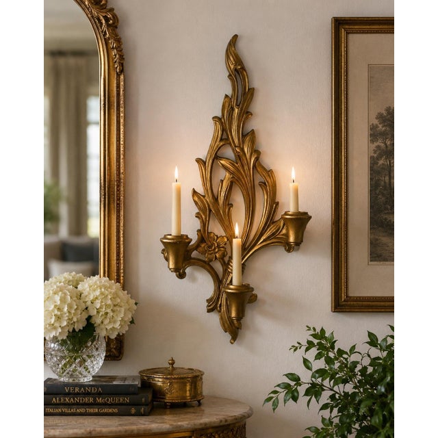 A striking vintage Hollywood Regency wall sconce featuring an ornate three-arm design with stylized acanthus leaves and...