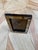 A tabletop picture frame with a border of rectangular tiles in warm cream, honey, and brown tones. Slim dark trim outlines...