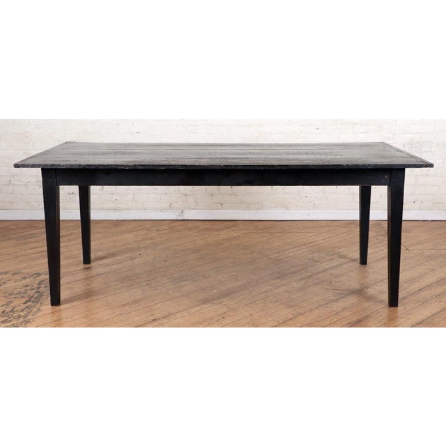 A beautiful worn primitive farmhouse dining table in worn and chipped black paint with four legs. Rare piece in a...