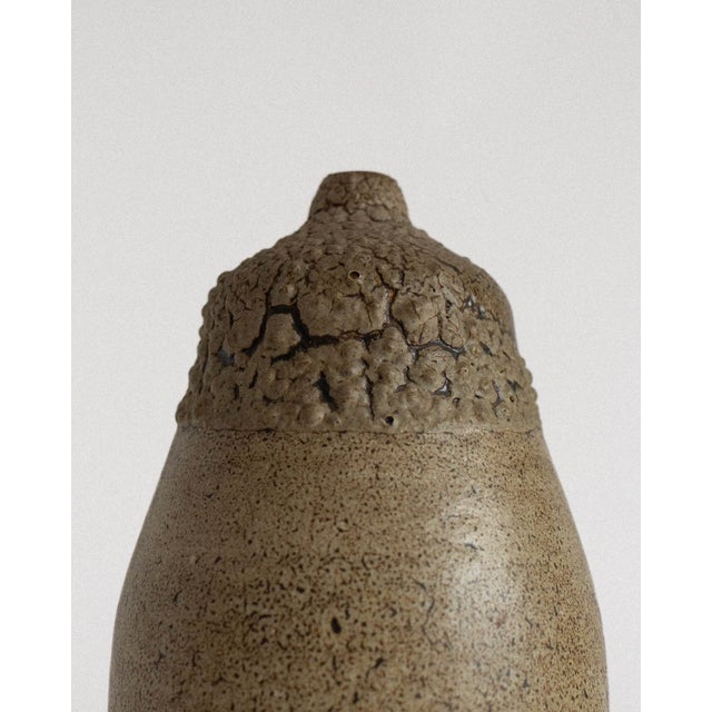 A single-stem ceramic vase with a tall, rounded body and a gently narrowed neck, defined by an exceptionally tactile...