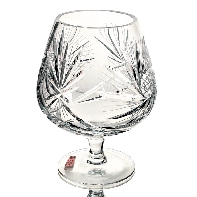 In the glass, light lingers, slipping through the pinwheel cuts like whispered secrets on porcelain air. This vessel is...