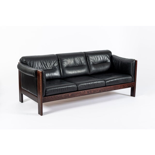 This vintage mid century Danish modern black leather three-seat sofa in the style of Arne Norell is circa 1970. This...