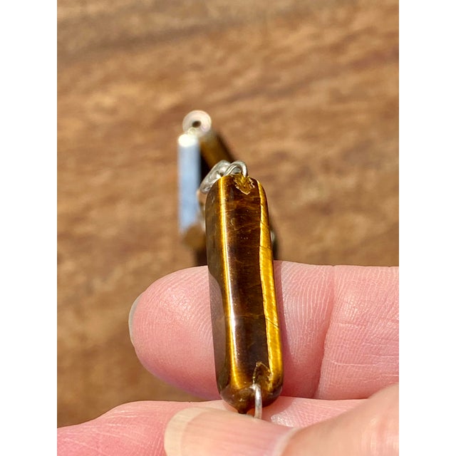 A striking blend of artistry and sophistication, this long necklace features intricately carved tiger eye gemstones...