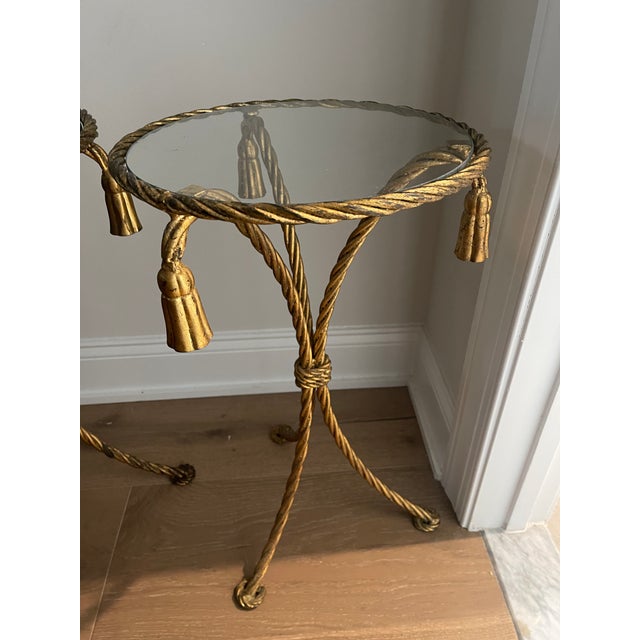 Mid-century pair of Italian gilded aluminum tables with the rope twist and tassel design. Each table has a glass insert....