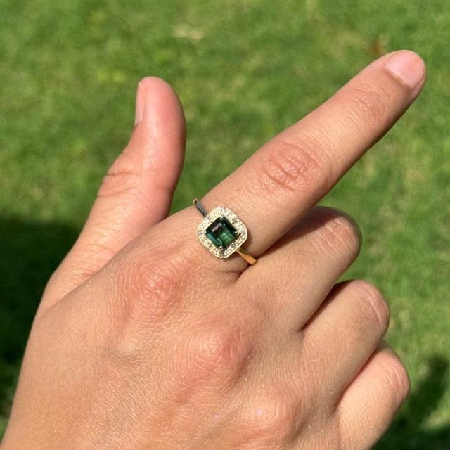 This Halo ring showcases a striking 1.22 carat green tourmaline set in 14K yellow gold. The tourmaline measuring 5.5 x 5.5...