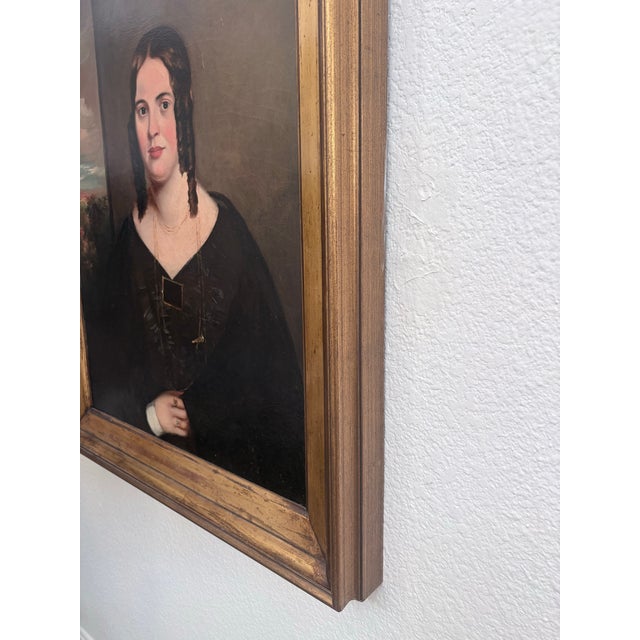 Striking 19th-century oil-on-canvas portrait of a young woman, presented in a substantial antique giltwood frame. The...