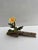 The artwork features a delicate flower emerging from a piece of driftwood, skillfully crafted from paper, wire, and paint....