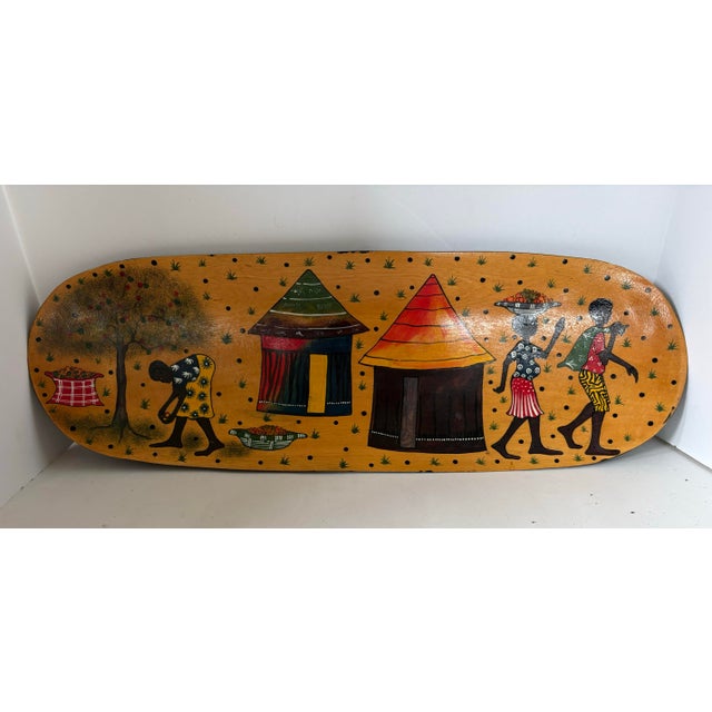 Hand-painted African folk art wall panel featuring a lively village scene with traditional huts and harvest figures. Rich...