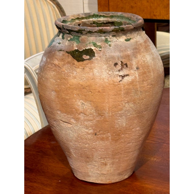 A French terracotta confit pot with a tapered body and thickened rim, showing areas of original green glaze remaining at...