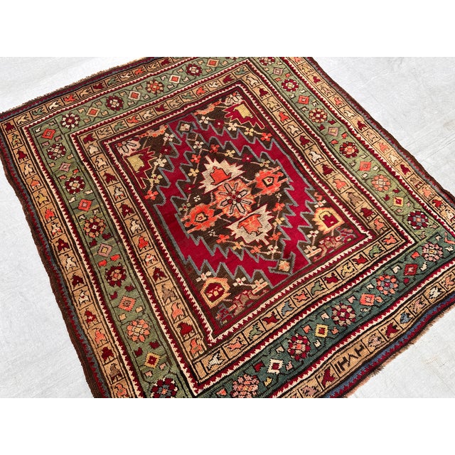 This antique hand-knotted Akstafa rug features a bold serrated diamond medallion in deep red and chocolate brown, framed...
